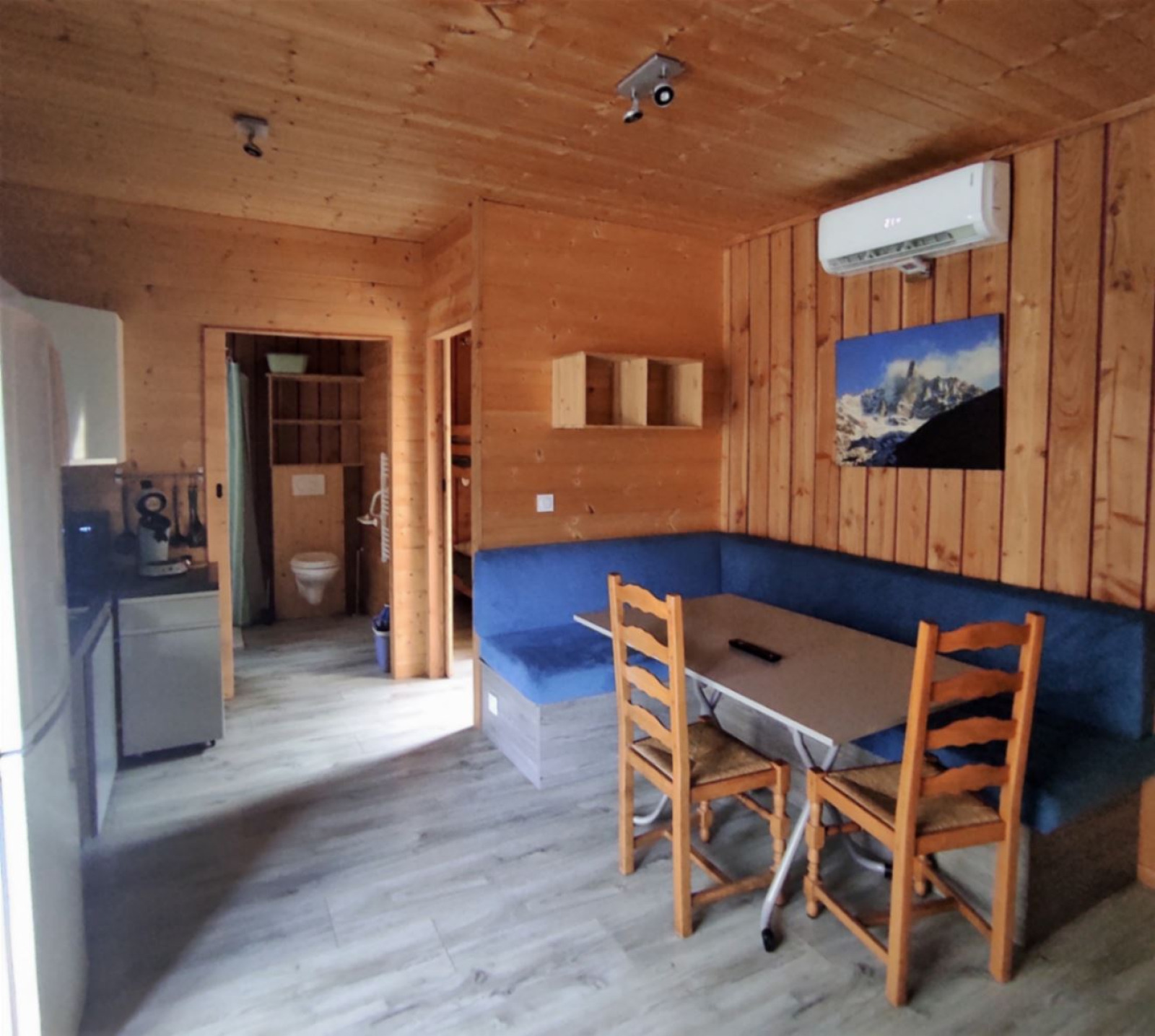 Interieur van chalet met houten wanden, blauwe zithoek, keuken en tafel, geschikt voor beperkte mobiliteit.