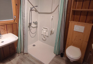 Accessible bathroom with walk-in shower, grab bars, fold-down shower seat, washbasin, and wall toilet.