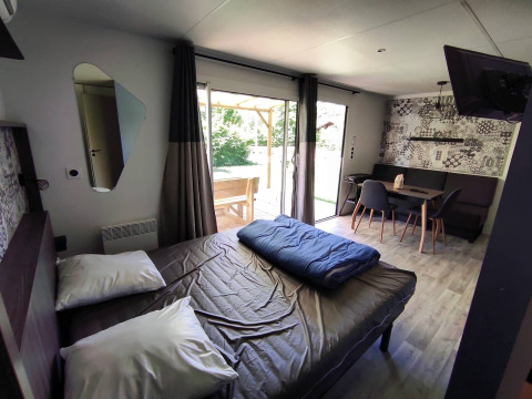 Modern glamping accommodation featuring a double bed, dining area, and large doors opening to a terrace.