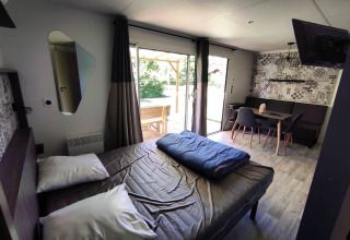 Hébergement glamping moderne avec lit double, coin repas et grandes portes vitrées donnant sur la terrasse.