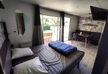 Alloggio glamping moderno con letto matrimoniale, zona pranzo e ampie porte verso la terrazza esterna.