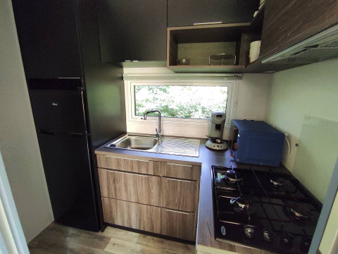 Cucina compatta da glamping con piano cottura a gas, lavello, macchina da caffè e frigorifero.