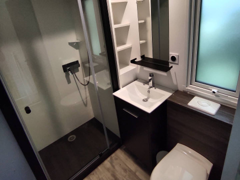 Modern bathroom at a glamping accommodation featuring a shower cabin, sink, toilet, and frosted window.