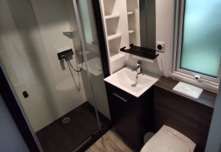 Bagno moderno in una sistemazione glamping con doccia, lavabo, WC e una grande finestra opaca.
