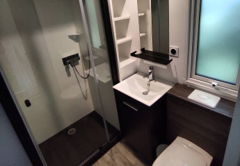 Modern bathroom at a glamping accommodation featuring a shower cabin, sink, toilet, and frosted window.