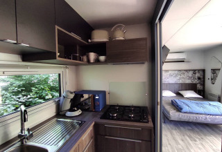Cuisine moderne et chambre dans une tiny house au Family's Camping Le Savoy, France, avec vue sur la verdure.