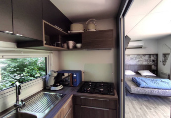 Moderne tekøkken og soveværelse i et lille hus på Family's Camping Le Savoy, Frankrig, med store vinduer.