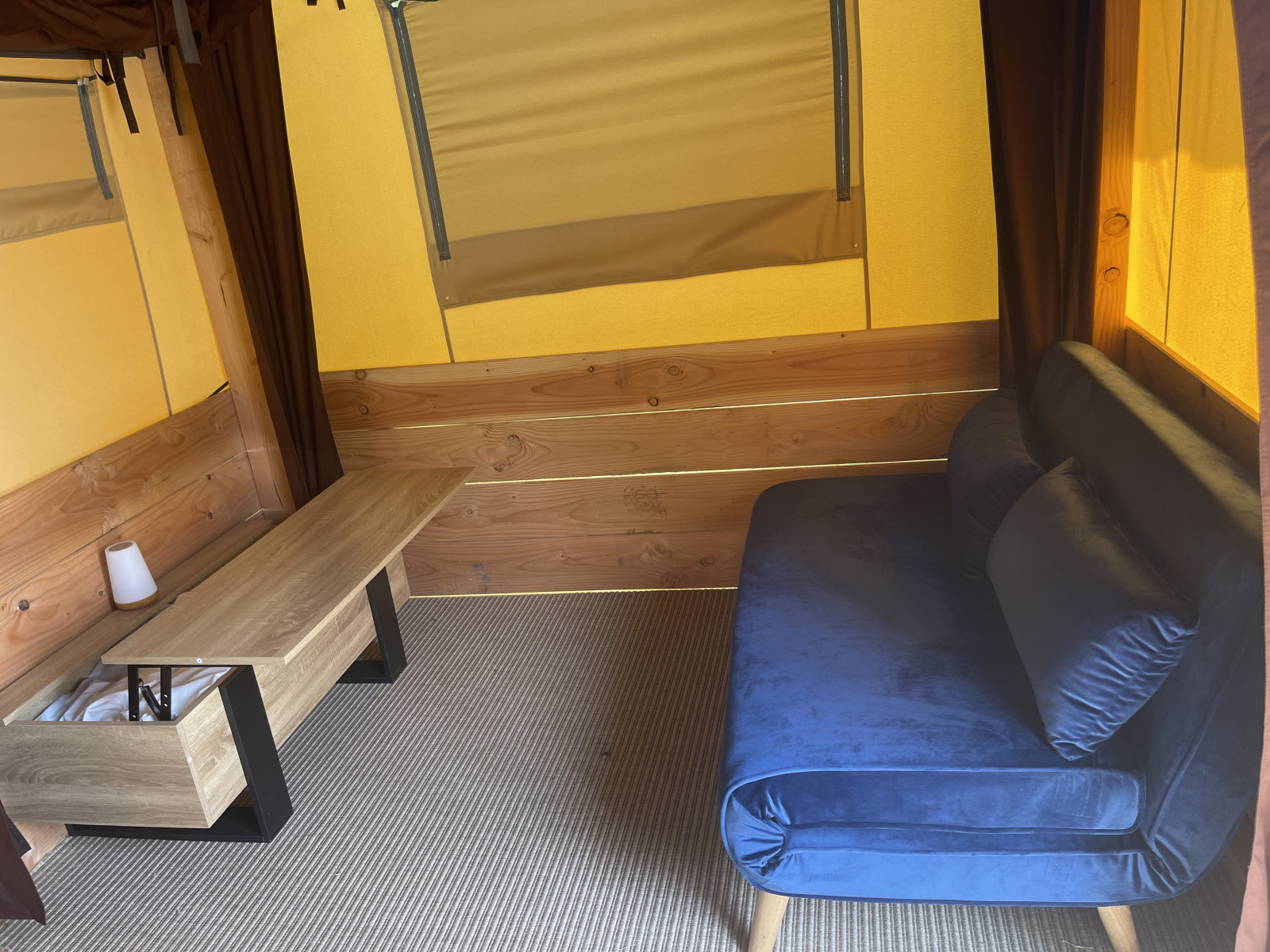 Interieur van de Avonturiers tent bij Camping Paradis Family des Issoux met blauwe bank en houten tafel.