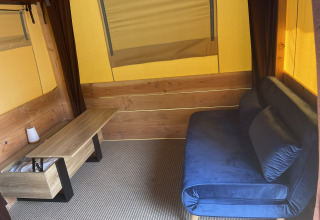 Interieur van de Avonturiers tent bij Camping Paradis Family des Issoux met blauwe zetel en houten tafel.
