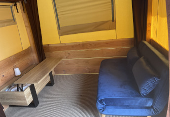 Interno della tenda Avonturiers al Camping Paradis Family des Issoux con divano blu e tavolo di legno.