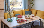 Essbereich mit gelben Kissen, gedecktem Tisch und Fenster in einem Mobilheim auf Camping Paradis Family des Issoux.