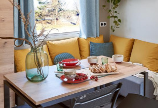 Eettafel met gele kussens, eten en raam in een Comfort Mobile home op Camping Paradis Family des Issoux.