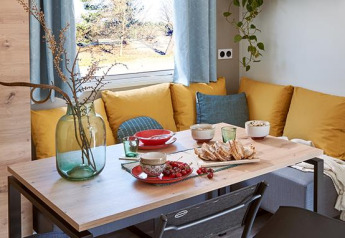 Mesa de comedor con cojines amarillos, comida y ventana en Comfort Mobile home de Camping Paradis Family des Issoux.