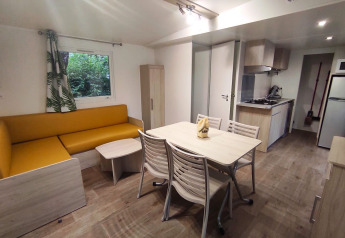 Foto interior de alojamiento glamping con sofá amarillo, mesa de comedor, pequeña cocina y ventana.