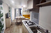 Moderne Glamping-Unterkunft mit Küchenzeile, Esstisch, Sofa, TV und Vorhängen mit Blättermuster.