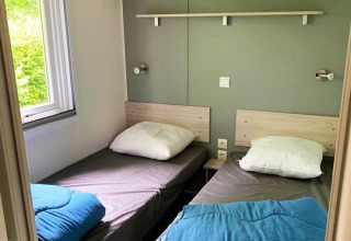 Twee eenpersoonsbedden met grijs beddengoed, blauwe dekens en witte kussens in een glampingkamer.