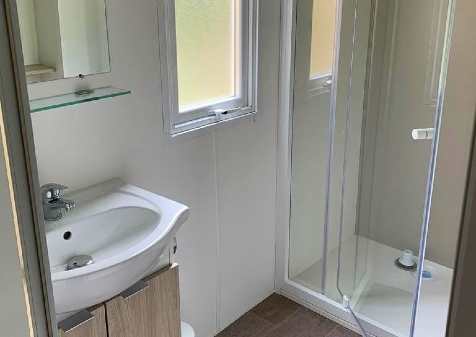Lichte glamping-badkamer met glazen douchecabine, modern wastafelmeubel en raam met daglicht.