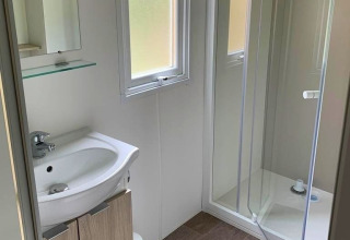 Salle de bain lumineuse en glamping avec douche vitrée, lavabo moderne et fenêtre laissant entrer la lumière.