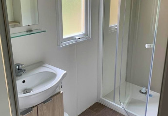 Baño luminoso de glamping con ducha de cristal, lavabo moderno y ventana que deja entrar luz natural.