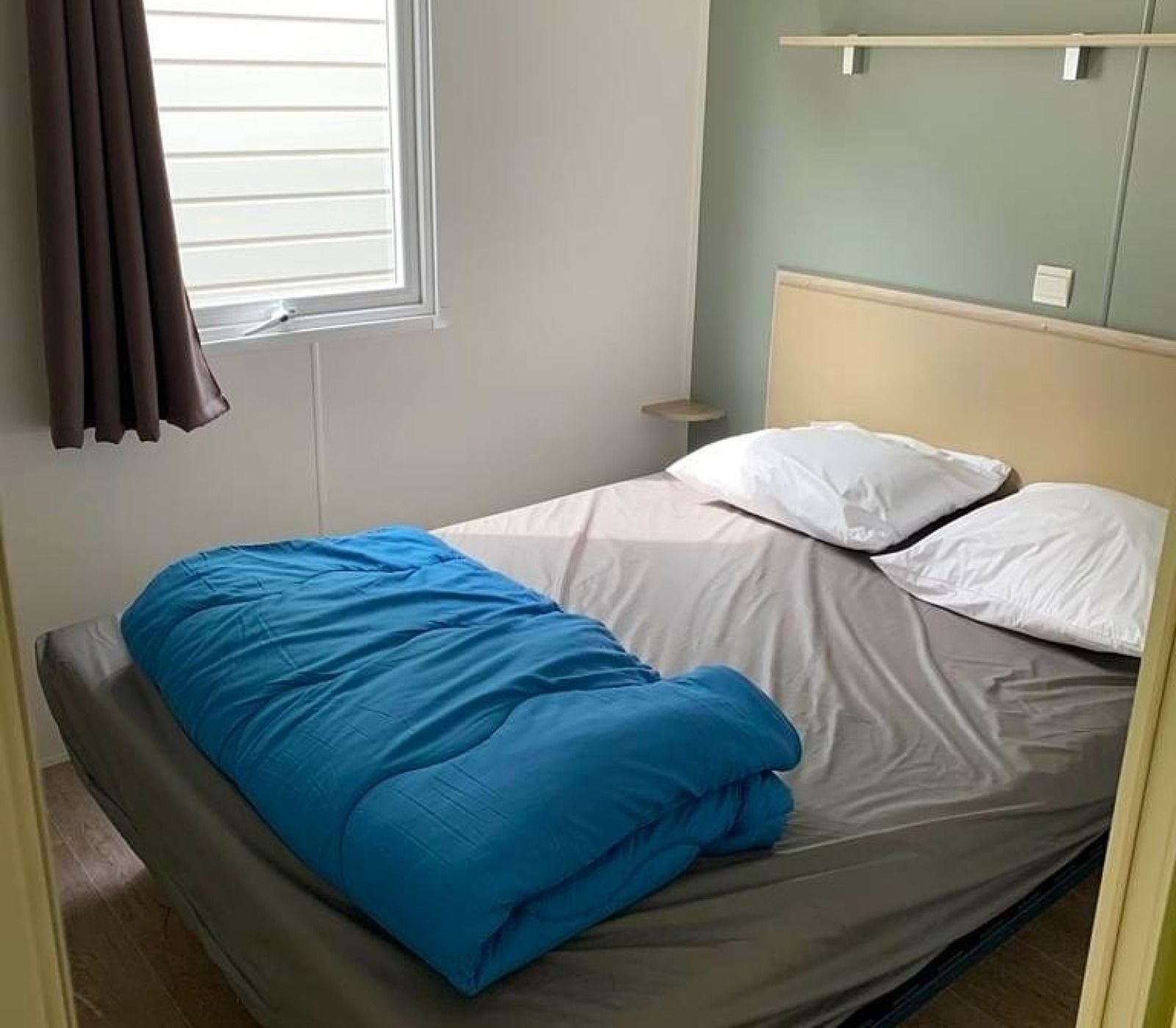 Glampingkamer met tweepersoonsbed, blauw dekbed, twee kussens, grijs laken en zijraam.