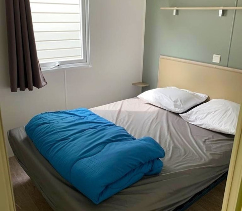 Glampingkamer met tweepersoonsbed, blauw dekbed, twee kussens, grijs laken en zijraam.