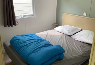Chambre en glamping avec un lit double, couverture bleue, drap gris, deux oreillers et une fenêtre latérale.