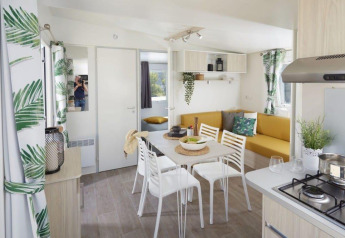 Helles Interieur des Comfort Mobile Home im Camping Paradis Family des Issoux mit Essbereich und Sofa.