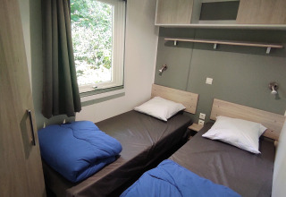 To enkeltværelser med blå dyner og et stort vindue i Stacaravan CONFORT på Family's Camping Le Savoy, Frankrig.