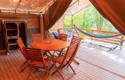 Terraza de madera con mesa, sillas y hamaca en una tienda safari en Flower Camping Provence Vallée, Francia.