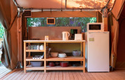 Cocina de tienda safari con estantería de madera, nevera y microondas en Flower Camping Provence Vallée.