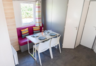 Zona pranzo nella Mobile Home «ECO Lodgia» al Flower Camping Provence Vallée, tavolo apparecchiato e cuscini vivaci.