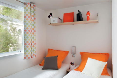 Modernes, farbenfrohes Zimmer mit zwei Betten, orangen Kissen und bunter Deko im Mobile Home «ECO Lodgia» in Frankreich.