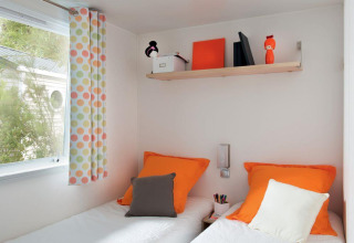 Modernes, farbenfrohes Zimmer mit zwei Betten, orangen Kissen und bunter Deko im Mobile Home «ECO Lodgia» in Frankreich.
