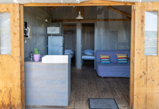 Interiør af Lodgehut op palen træhus med sofa, tekøkken og seng på Flower Camping Provence Vallée, Frankrig.