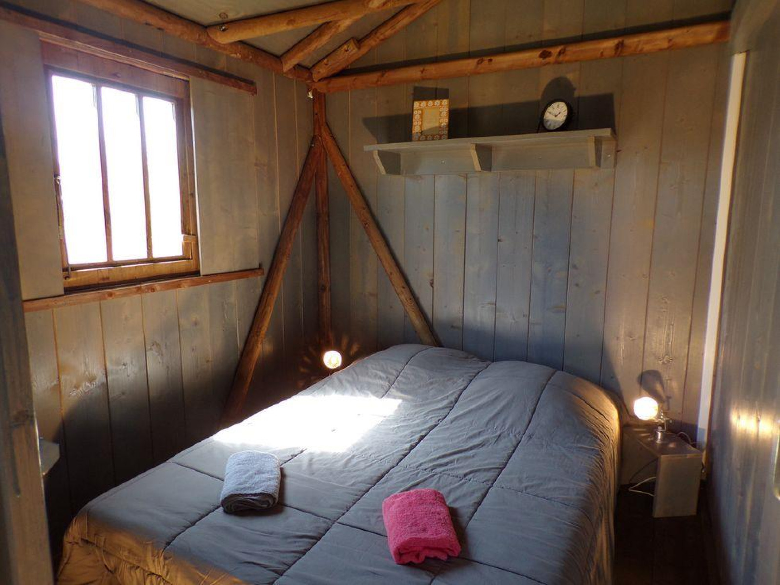 Slaapkamer met houten muren en balken in lodgehut op palen bij Flower Camping Provence Vallée, Frankrijk.