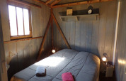 Schlafzimmer mit Holzwänden und rustikalen Balken in einer Baumhütte bei Flower Camping Provence Vallée, Frankreich.