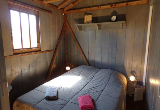 Cozy bedroom with wood-paneled walls in the tree house 'Lodgehut op palen' at Flower Camping Provence Vallée, France.