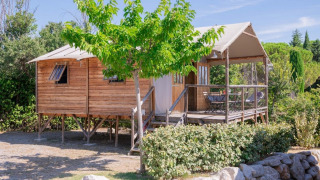 Vista esterna della casa sull'albero Lodgehut op palen su palafitte, circondata dal verde e cielo sereno.