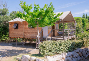 Vista esterna della casa sull'albero Lodgehut op palen su palafitte, circondata dal verde e cielo sereno.