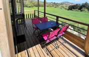 Terraza de madera cubierta con sillas rosas y mesa negra en Mobile Home «Living» de Flower Camping Provence Vallée, Francia.