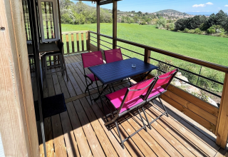 Terrasse en bois couverte avec chaises roses et table noire au Mobile Home «Living» du Flower Camping Provence Vallée, France.