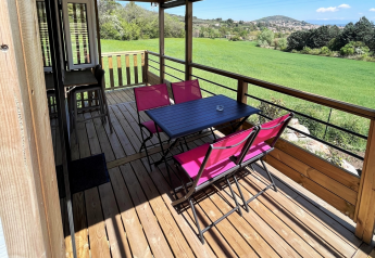 Overdækket træterrasse med pink stole og sort bord på Mobile Home «Living» i Flower Camping Provence Vallée, Frankrig.