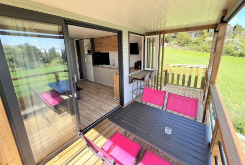 Mobil-home Living au Flower Camping Provence Vallée avec terrasse, chaises roses et vue sur pelouse.