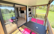 Mobil-home Living au Flower Camping Provence Vallée avec terrasse, chaises roses et vue sur pelouse.