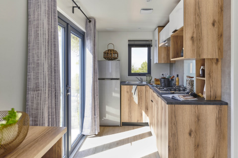 Cucina moderna con mobili in legno e grandi finestre presso Mobile Home «New Horizon» al Flower Camping Provence Vallée.