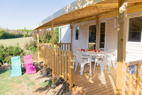 Mobil-home avec terrasse en bois, chaises blanches et transats au Flower Camping Provence Vallée en France.