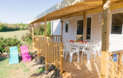 Mobilheim mit Holzterrasse, weißen Kunststoffstühlen und Liegestühlen bei Flower Camping Provence Vallée.