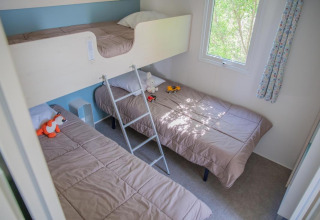 Camera per bambini con letto a castello, due letti singoli, giocattoli sui letti e finestra vista alberi.