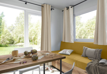 Lyst opholdsrum i en Premium Mobile Home med stor sofa, spisebord og udsigt til en grøn have i Frankrig.