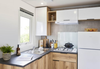 Cocina moderna en casa móvil Premium con armarios de madera, estufa de gas y nevera en Flower Camping Provence Vallée.